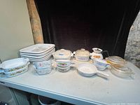 Wide view of entire lot showing multiple ceramic and glass cookware in vintage CorningWare patterns such as Spice of Life and Cornflower Blue, including lasagna pans, casseroles, skillets, and teapot.