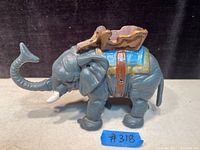 Side view of one gray cast iron elephant figurine with a blue saddle and brown wooden seat detail on top, with its trunk raised.