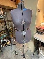 Front view of black dressmaker's form with three adjustment dials and metal stand in workshop area.