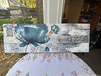 Large horizontal oil painting on canvas showing abstract blue flowers on mixed neutral textured background.