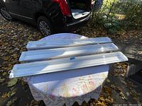 Three white LED light fixtures placed on a round table outdoors. Each fixture is long and slim, approximately 47 inches in length and 6 inches wide. The lights appear to be clean and in very good condition.