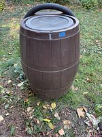 Full view of the brown plastic rain catcher barrel standing outdoors with a flexible hose looped over the top.
