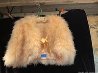 Photo of vintage pink feather jacket hanging against black background showing fluffy feathers and cream satin lining underneath.