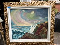 Full view of the framed oil painting showing the coastal scene with waves and colorful sky.
