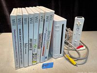 Front view of all 8 Wii game cases and the Nintendo Wii console with Wii Remote and AV cable, showing titles and condition.
