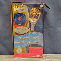 Front view of the boxed Barbie doll featuring the Olympic swimming champion theme with visible minor storage damage on the box.