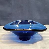 Side view of the deep blue art glass dish showing the rounded base and flared rim with black edging.