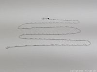 Full view of the 28-inch long sterling silver rope chain necklace laid out in a loose zig zag pattern on a white background.