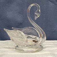 Full view of the clear crystal swan figurine positioned on a light surface with a dark background, showing the full body and etched wing details.