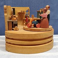 Photo of round wooden music box base with Santa's workshop scene including two wooden figurines and assorted miniature woodworking tools and toy wood items.
