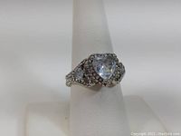 Close-up of heart-shaped centerpiece stone with side stones and band details on white display stand.