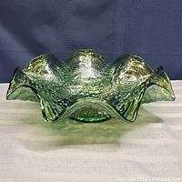 Side view of the green carnival glass dish showing wavy edges and textured grapes and leaves design.