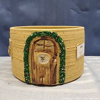 Full view of circular pottery bowl showing textured brick-like exterior and decorative door with green leafy arch design