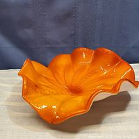 Side angled view showing the ruffled, wavy orange and white art glass dish with glossy finish and textured surface.