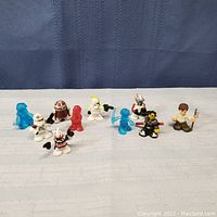 Array of 12 mini Star Wars figurines including R2D2, clone troopers, and translucent blue droids arranged on a cloth surface.