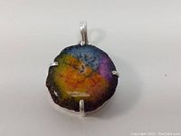 Close-up front view of round rainbow agate pendant with colorful concentric bands, natural rough edges, and silver prong setting.