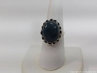 Photo of sterling silver ring with dark blue oval stone on white ring stand, front view.
