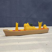 Side view of the Tootsietoy plastic cargo ship model showing beige hull, red deck, and yellow superstructures and cranes.