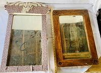 Two antique mirrors side by side on a flat surface, one oak framed with beveled glass and one with a decorative painted frame