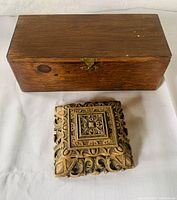 Rectangular plain wood box and smaller heavily carved rosewood box placed on fabric surface, showing top and sides of both boxes with latch visible on larger box.