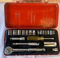 View of the Mastercraft 20-piece socket set open inside a red metal case, showing the ratchet, various sockets, screwdriver handle, extension bar, and other accessories held in a black molded tray.
