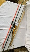 Three longbows laid on white surface: one wooden traditional recurve bow with natural finish, one black Titan children's bow, and one red Titan children's bow.