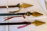 Three vintage wooden staffs with copper spearheads and fabric ribbons on a cloth background
