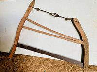 Antique wooden frame buck/bow saw with visible metal blade and tension mechanism on a floor background.
