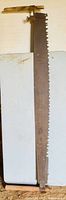 Full view of the antique crosscut saw with metal blade and rectangular wooden handle affixed with clamp.