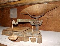 Side view of antique cast iron platform scale showing the pan, platform, and weight scale beam with several rusty metal weights in front.