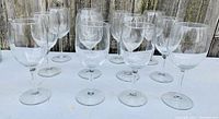 Twelve clear stemmed wine glasses arranged in rows on a white surface with a wooden fence background; front view
