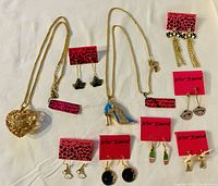 Photo showing Betsy Johnson large heart pendant necklace, blue high heel shoe pendant necklace, and seven pairs of matching earrings on branded display cards.