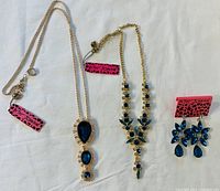 Four piece Betsy Johnson jewelry set including two necklaces and a pair of earrings with blue and green crystals on gold-tone metal.
