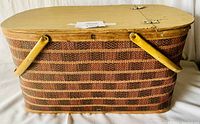 View of the large woven picnic basket with two yellow wooden handles and hinged wooden lid showing side and top.