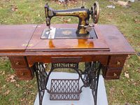 Front view of vintage Singer treadle sewing machine mounted in an oak cabinet showing machine, drawers, treadle and pedal.