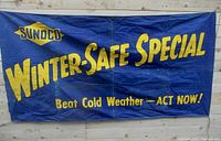 Full view of the Sunoco Winter-Safe Special banner hanging on wooden wall, showing the blue canvas material and yellow lettering.