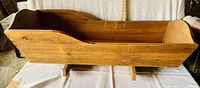 Photo shows handcrafted solid pine wooden doll cradle with visible wood grain and curved ends, placed against a cloth background.