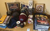 Full overview of all items on table, showing multiple Broncos caps, mugs, books, bobbleheads, and plaques