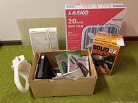 Photo showing a Lasko 20 inch box fan in its original box, Solid Ox welding rods box, and an open cardboard box containing various miscellaneous items.