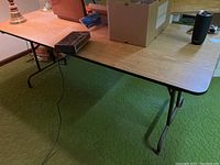 Side angle view of the 6 ft metal folding table showing the laminate wood-look top and metal folding legs attached with hinges.