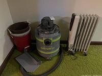 Full shot showing Genie Jet Vac vacuum cleaner with attached hose, two buckets, and heater beside them on green carpet.