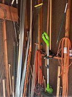 Photo showing the Greenworks electric string trimmer hanging on the wall with other garden tools including the hatchet and sledge hammer.
