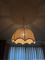 Woven rattan dome-shaped swag lamp suspended from ceiling, lit and showing intricate shadow patterns on ceiling.