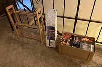 Two wooden media racks, one assembled and one boxed, with cardboard box of DVDs beside them