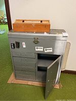 Front view of gray metal tool chest with seven drawers, side cabinet door open, and wooden Starrett precision level on top.