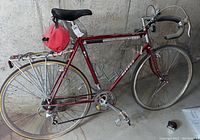 Full side profile of the vintage Miyata touring road bike showing red frame, rear luggage rack with red saddle bag, and drop handlebars.