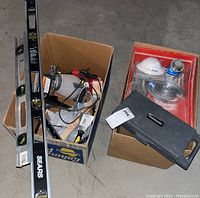 Two cardboard boxes filled with hand tools, painting supplies, and equipment; two Sears branded metal levels leaning on boxes; FireMark socket set case atop one box; respirator mask and spray paint can visible; shot to show overall lot contents.