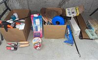 General view of two boxes containing painting supplies and plumbing tools on a basement floor.