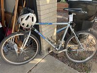 Side view of silver Raleigh Technium mountain bike with helmet mounted on handlebars, leaning against brick wall outside.
