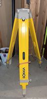 Full view of yellow Sokkisha survey tripod standing on concrete floor with visible pointed feet and carry strap.